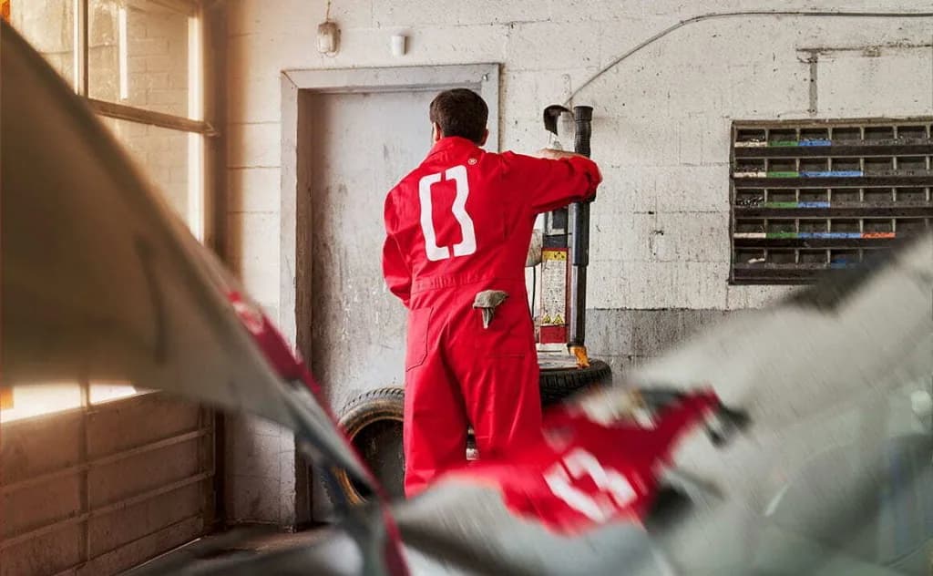 Mécanicien de dos, en combinaison rouge, dans un garage.