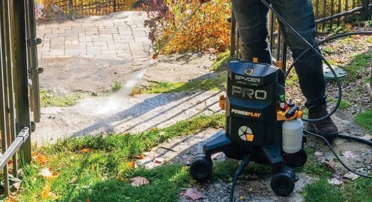 Personne qui lave un patio de pierre avec une laveuse à pression sur roues.