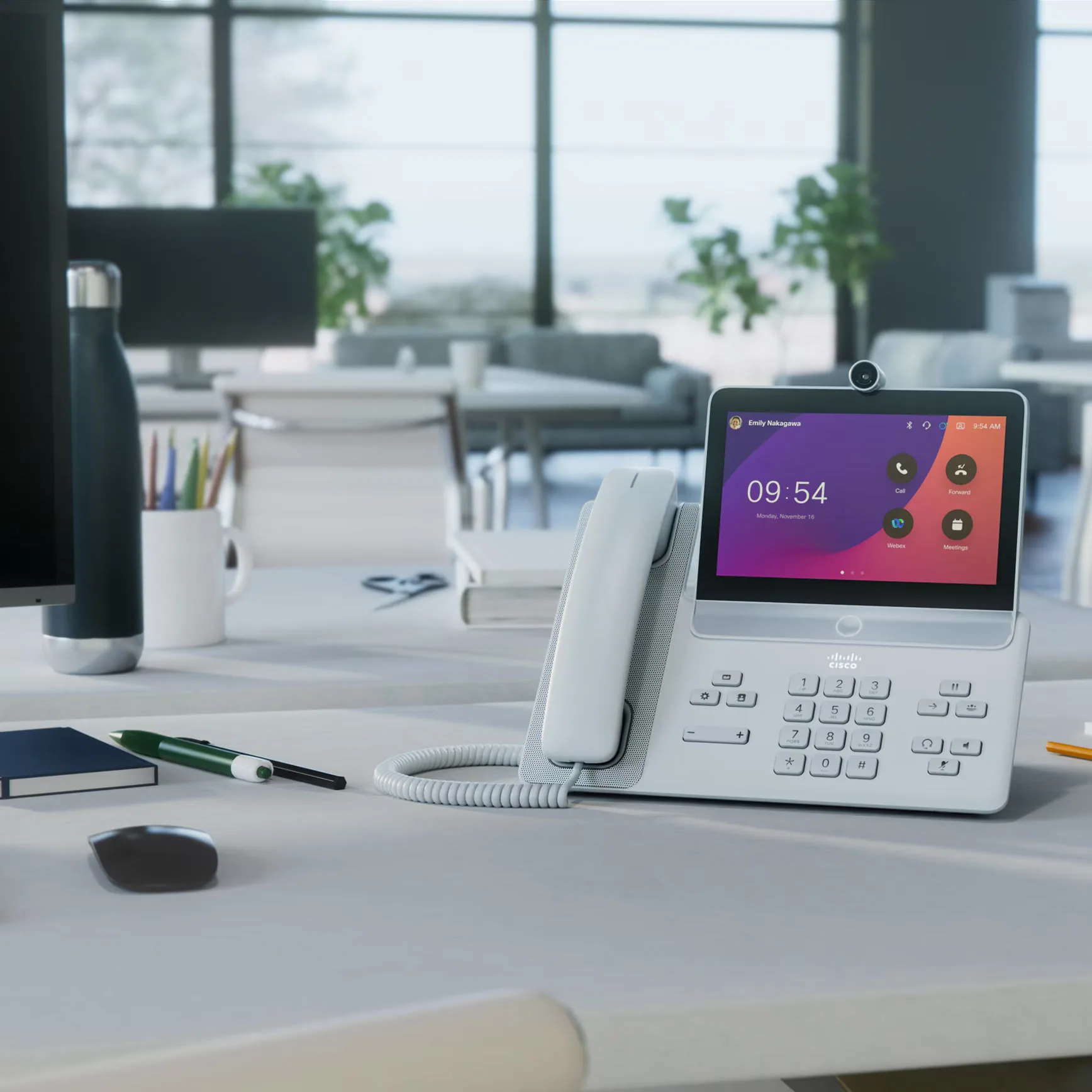 White desk phone with a color screen, on an office desk by a window.