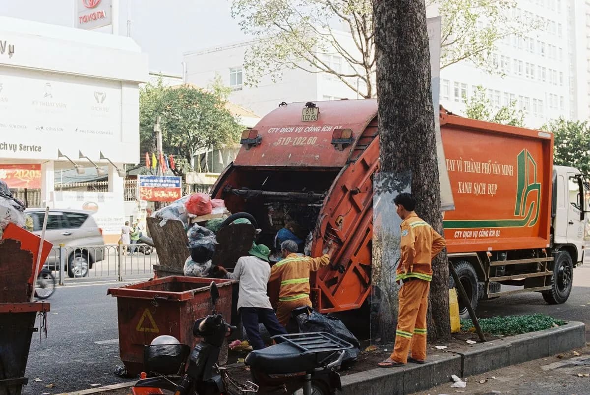 Camion de collecte des déchets et employés ramassant les ordures dans une rue urbaine.